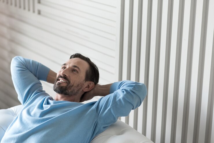 Foto sendo feliz. homem alegre com boa aparência positiva, segurando as mãos atrás da cabeça e olhando para cima enquanto relaxa no sofá