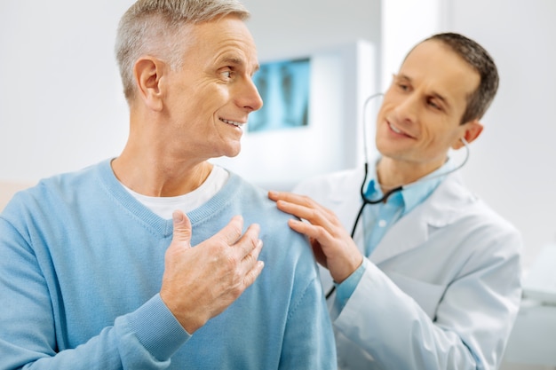 Sendo otimista. Homem alegre e feliz sorrindo e se voltando para o médico enquanto se sente otimista