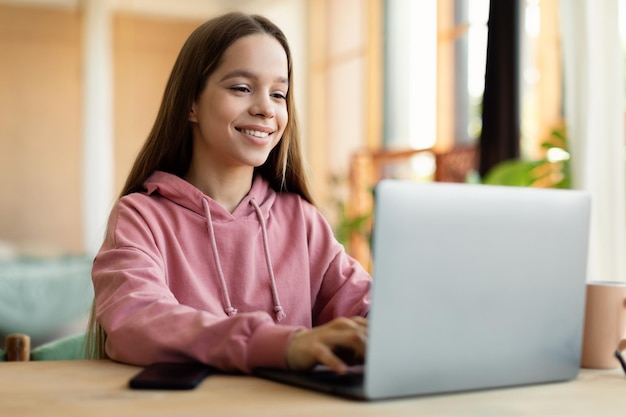 Foto senhora adolescente feliz digitando no laptop estudando online em casa sentado à mesa no interior da sala de estar