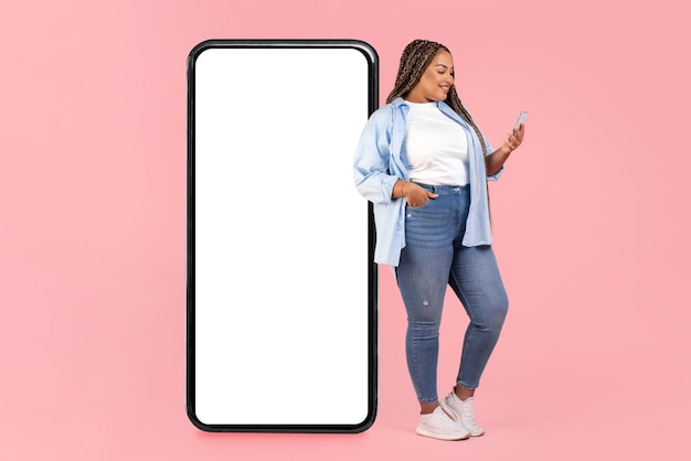 Senhora africana, apoiando-se em mensagens de texto de telefone grande sobre fundo rosa