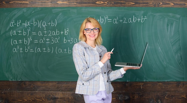 Senhora alegre educadora com laptop moderno navegando na internet fundo de lousa A educação é divertida A professora usa óculos segura laptop navegando na internet Conceito de tecnologias digitais