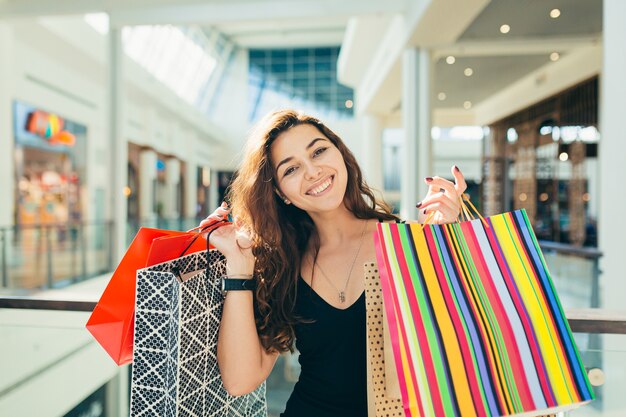 Senhora alegre em um vestido preto elegante, carregando sacolas de compras coloridas enquanto caminha pela loja