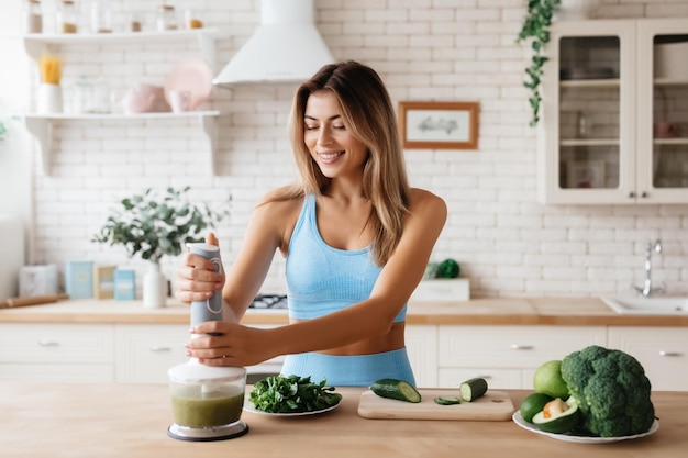 Senhora alegre no top azul usando liquidificador para fazer um bom smoothie fresco