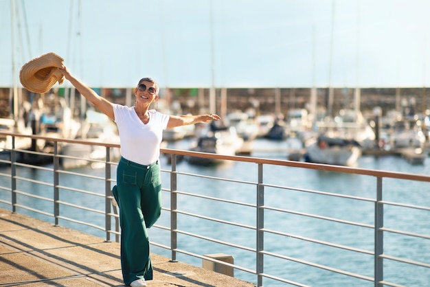 Senhora alegre posando com chapéu e se divertindo na marina