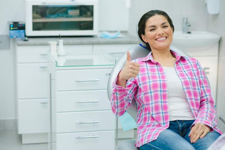 Senhora animada colocando o polegar para cima e sorrindo com dentes brancos revelados enquanto está sentada em uma cadeira odontológica. Banner do site