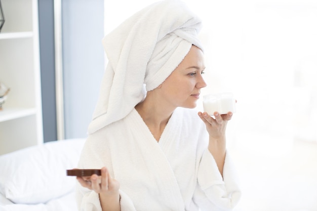 Senhora após o banho, segurando o creme facial na mão em casa