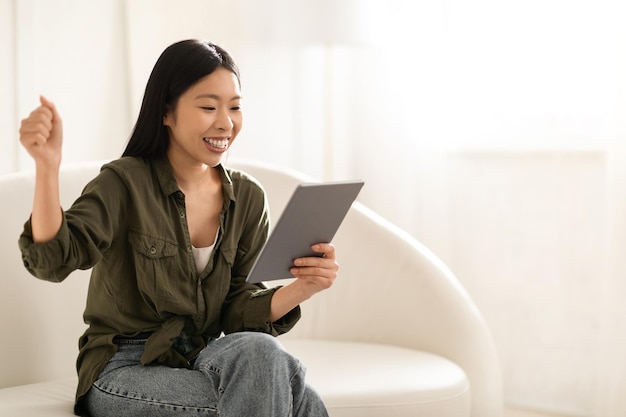 Senhora asiática emocional sentada no sofá com espaço de cópia de tablet