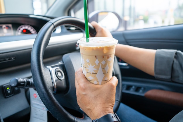 Senhora asiática segurando gelo café no carro.