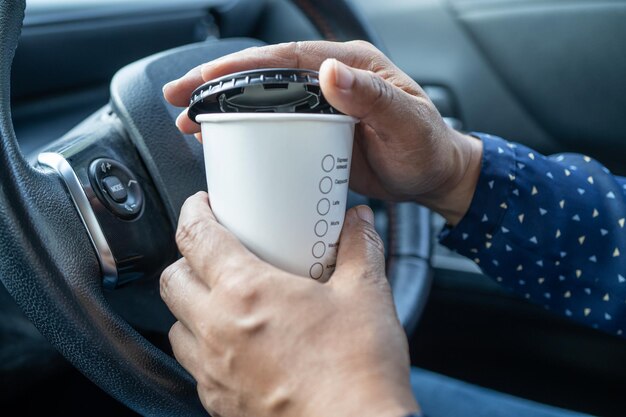 Senhora asiática segurando uma xícara de café quente para beber no carro perigoso e arriscar um acidente