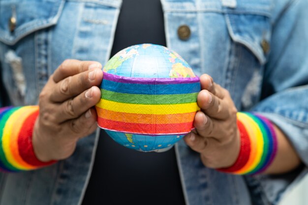 Foto senhora asiática vestindo jaqueta jeans azul ou camisa jeans e segurando uma bandeira da cor do arco-íris com o símbolo do globo do mês do orgulho lgbt