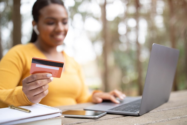 Senhora brasileira de pagamento on-line com laptop e cartão de crédito sentado ao ar livre desfrutando de internet banking