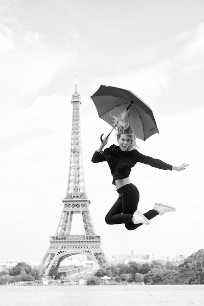 Senhora com guarda-chuva animada em visitar o fundo do céu da torre eiffel senhora turista esportiva e ativa no centro da cidade de paris pula menina turista gosta de passear e passear sonhos se tornam realidade