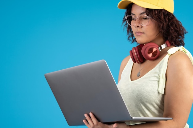 Senhora com óculos e um boné se concentrando enquanto trabalha em um laptop usando fones de ouvido