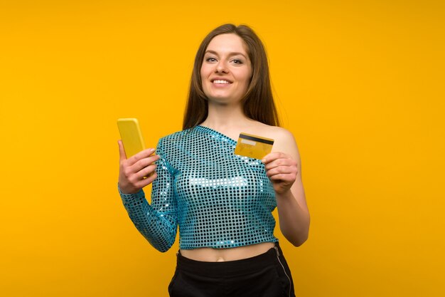 Foto senhora comprando online com um cartão de crédito e um smartphone em fundo amarelo