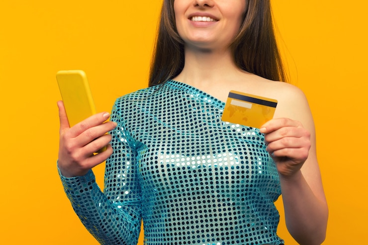 Foto senhora comprando online com um cartão de crédito e um smartphone em fundo amarelo