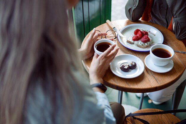 Senhora de cabelos grisalhos tomando uma xícara de café e passando um tempo com um amigo em um café aconchegante