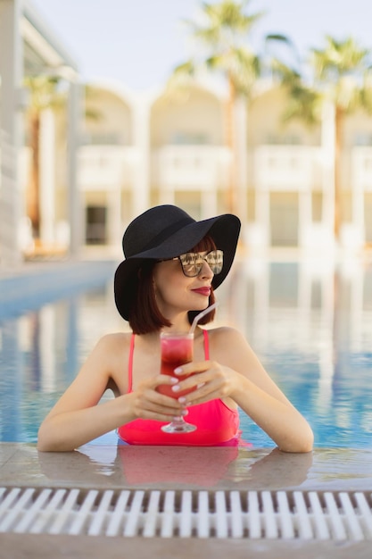 Senhora de maiô rosa na piscina do resort nadando e desfrutando de uma refrescante bebida gelada