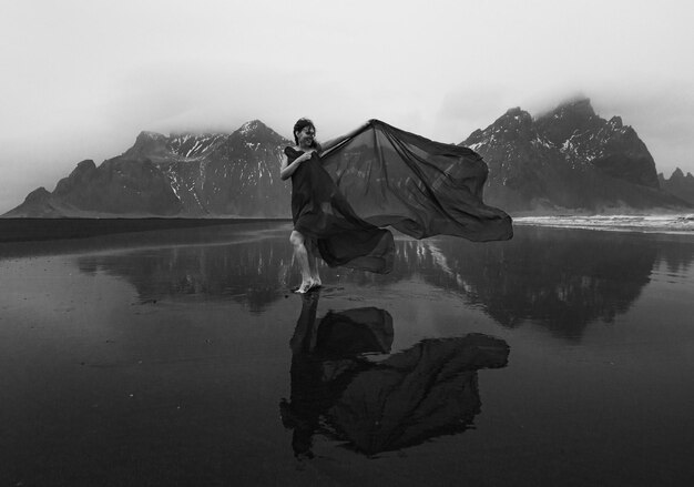 Senhora elegante envolta com chiffon na fotografia cênica monocromática de praia