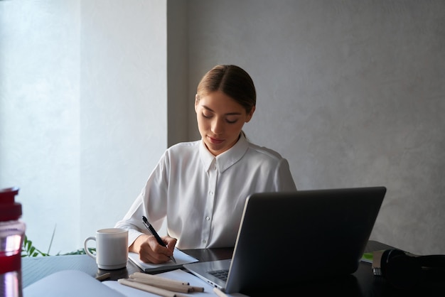 Senhora encantadora sentada à mesa e usando laptop sem fio