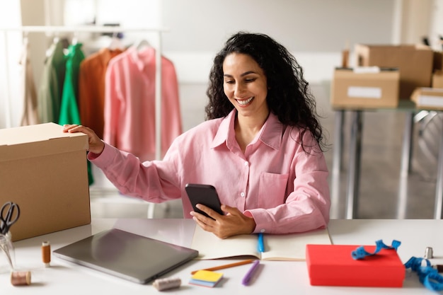 Senhora enviando mensagens de texto em caixas de embalagem de smartphones na loja de showroom de roupas