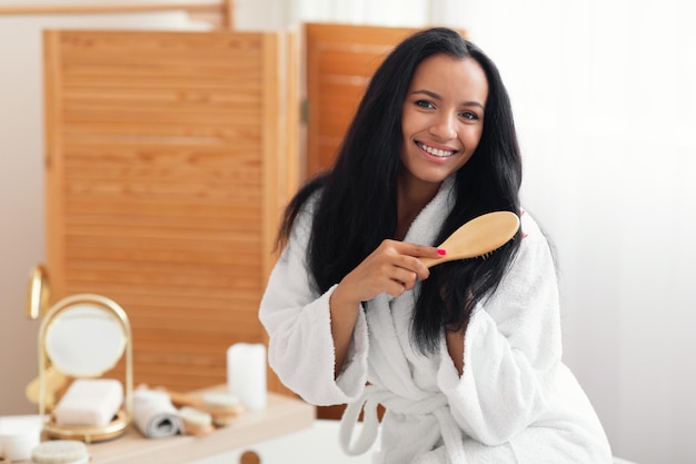 Senhora escovando o cabelo sorrindo para a câmera usando escova no banheiro