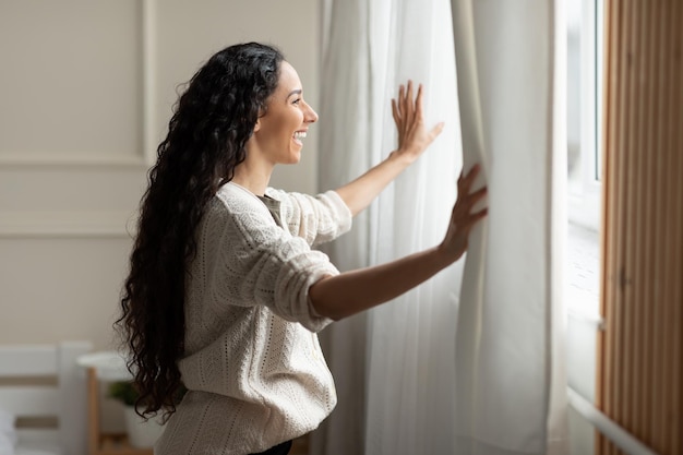 Senhora excitada abrindo as cortinas da janela em casa