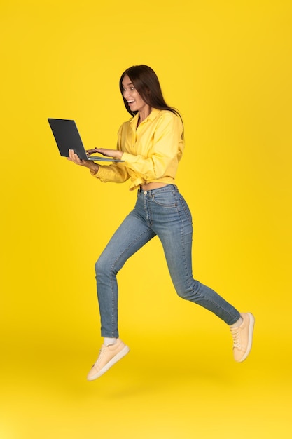 Senhora excitada usando laptop correndo posando sobre fundo amarelo vertical