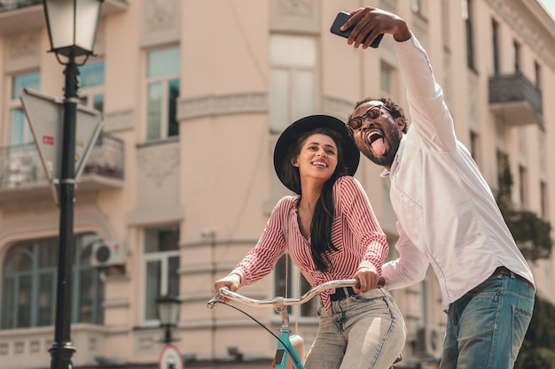 Senhora feliz andando de bicicleta e seu homem tirando uma selfie e mostrando a língua