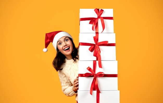 Senhora feliz com chapéu de Papai Noel segurando presentes em fundo amarelo