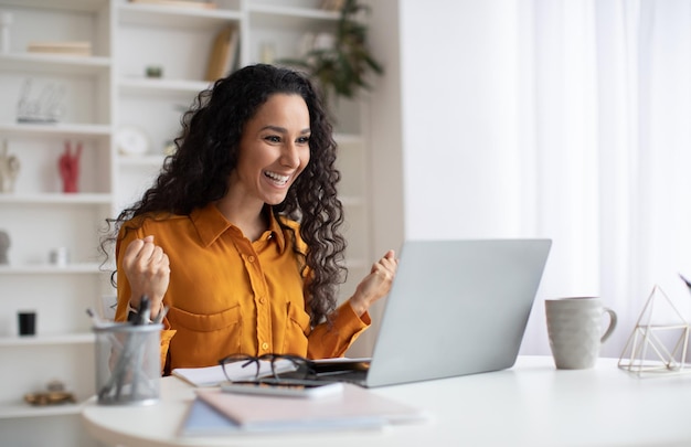 Senhora feliz usando laptop e gesticulando sim trabalhando no escritório