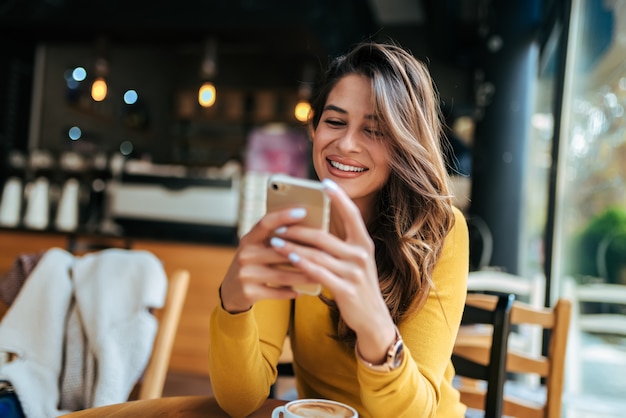 Foto senhora feliz usando telefone celular no café.