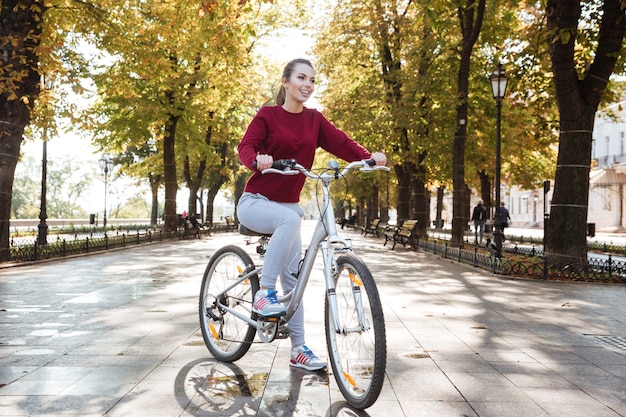 Senhora feliz vestida com um suéter caminhando com sua bicicleta ao ar livre