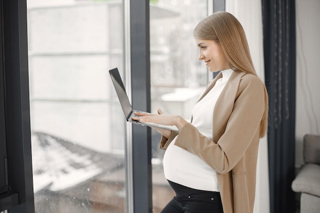 Senhora grávida digitando em um laptop em pé no escritório moderno