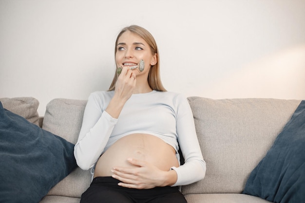 Senhora grávida sentada em um sofá na sala segurando um massageador de rosto