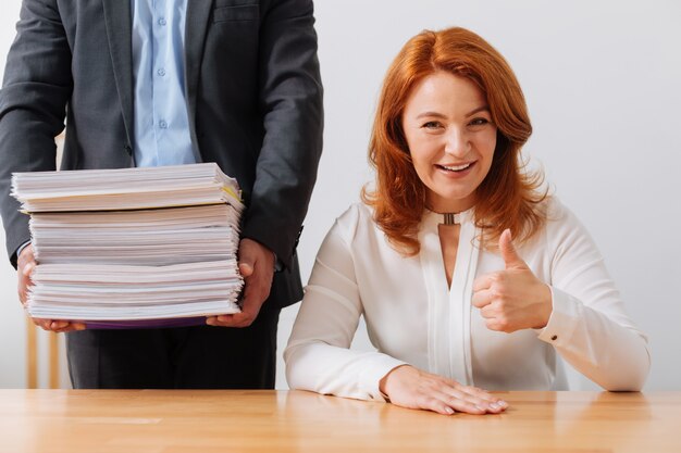 Senhora inteligente e admirável sentada em seu local de trabalho e recebendo uma pilha de documentos para sua consideração