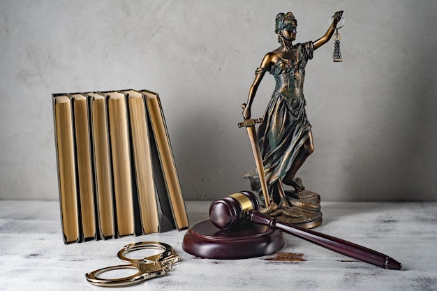 Senhora justiça, martelo do juiz, livros, algemas em uma velha mesa de madeira