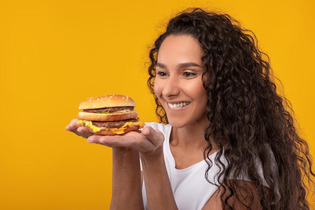 Senhora latina engraçada segurando hambúrguer no estúdio