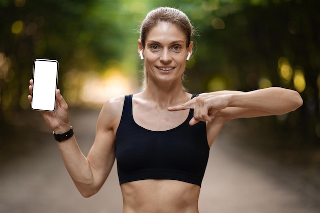 Senhora loira desportiva positiva mostrando smartphone com tela vazia