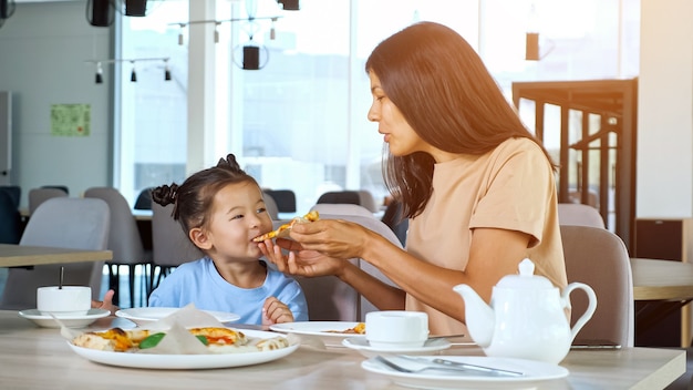 Senhora mãe segurando uma fatia de pizza e filha comendo no café