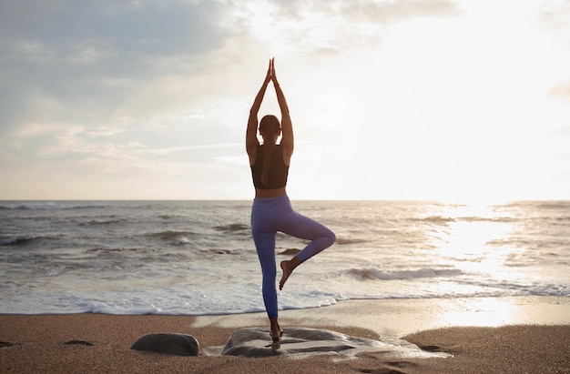 Senhora magra caucasiana do milênio pratica ioga desfruta de treino sozinha na praia do mar nas costas reflexo do sol