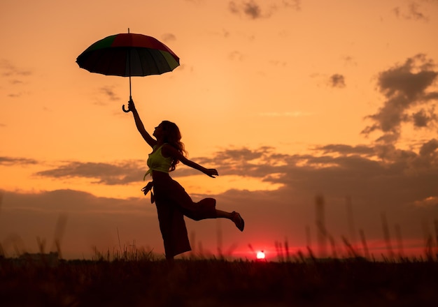 Senhora magro com guarda-chuva se divertindo durante o pôr do sol