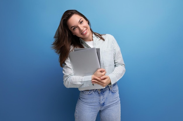 Senhora morena de sucesso em camisa e jeans segurando papéis e laptop de trabalho