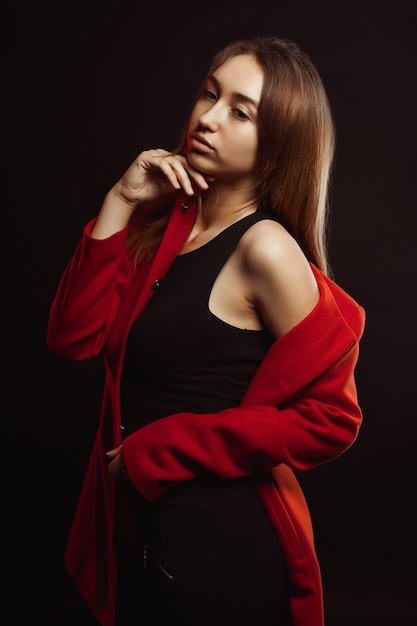 Senhora morena elegante com maquiagem natural e cabelo brilhante, posando com um casaco vermelho da moda no estúdio