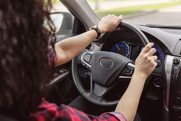 Senhora morena está segurando as mãos atrás do volante do carro.