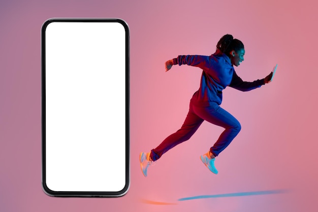 Foto senhora negra ativa se exercitando com celular ao lado de smartphone gigante com maquete de tela branca em branco