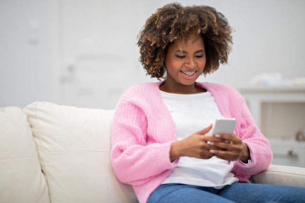 Senhora negra feliz sentada no sofá com espaço para cópia de smartphone