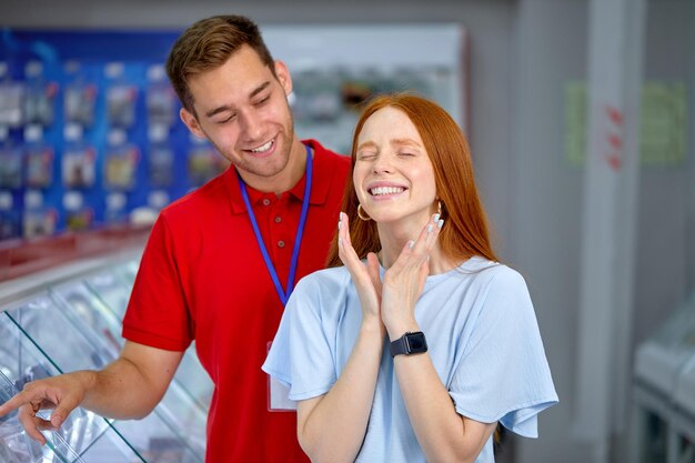 Senhora ruiva bonita em roupas casuais fica nas prateleiras com smartphones, com consultor