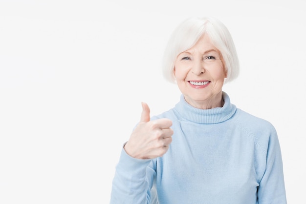 Senhora sênior mostrando o polegar para cima gesto sorrindo em fundo branco