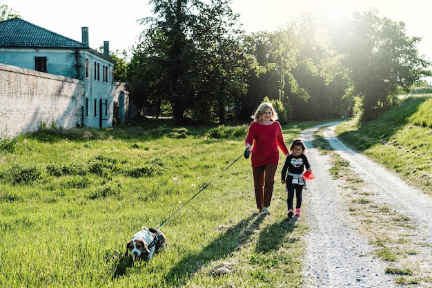 Senhora sênior na moda e sua garotinha desfrutando de um passeio no campo com seu cachorro beagle Avó e neta felizes juntos no parque em dia ensolarado Conceito de relacionamento