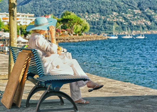 Senhora sênior sentada no banco no aterro no luxuoso resort Ascona no Lago Maggiore, cantão de Ticino, Suíça.